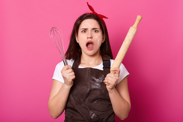 Impressed surprised brunette young female stands with wide opened mouth and eyes, holding cooking...