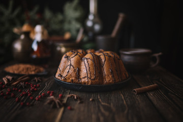 Holiday cake on wooden table with berry, spice and chocolate at rustic home kitchen. Christmas baking background. Ingredients for cooking on dark wooden background. Homemade festive food. Toned image