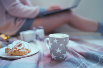 Winter hot drinks. Close up cup of coffee or hot chocolate. Blurred image womam in warm pink sweater with laptop, home comfort and relax. Christmas holidays, hot drinks and people concept.