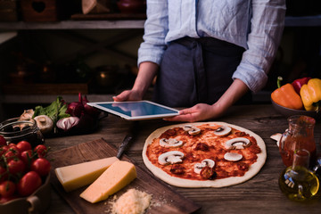 Cook hands. Close up on hands, some ingredients around on table. Fresh original Italian raw pizza, preparation in traditional style. Ingredients and spices for making homemade pizza on wooden table.