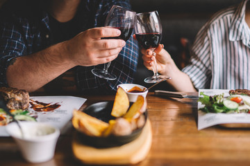 Glasses of red wine with food on table. Selective focus, couple toasting with glasses of red wine in the restoran. Blurred abstract background of clinking glasses of wine. Selective focus. Toned image