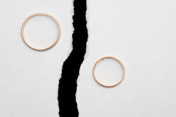 Wedding rings on different halves of a torn sheet of white paper.