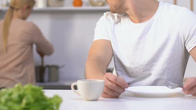 Hungry impatient husband holding knife and fork waiting for meal from slow wife