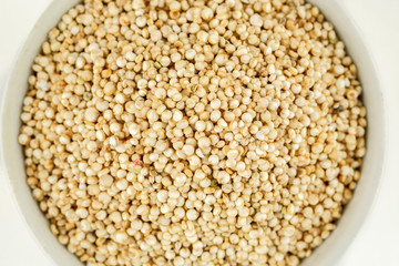 Quinoa raw seeds in white ceramic bowl on a white, macro shot, top view