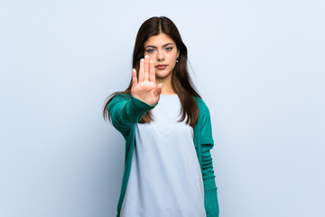 Teenager girl over blue wall making stop gesture