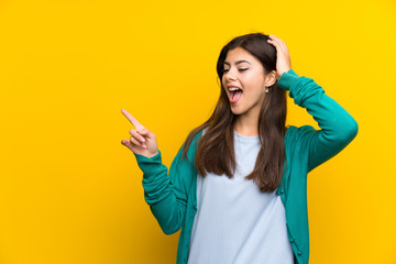 Teenager girl over yellow wall pointing finger to the side and presenting a product