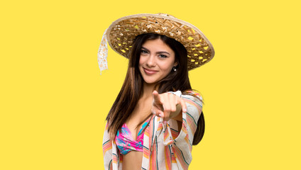 Teenager girl on summer vacation points finger at you with a confident expression over isolated yellow background