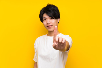 Asian man over isolated yellow wall showing and lifting a finger