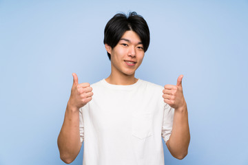 Asian man on isolated blue background giving a thumbs up gesture