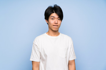 Asian man on isolated blue background having doubts and with confuse face expression