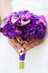 Beautiful wedding bouquet of purple freesia and red callasin the hands of the bride