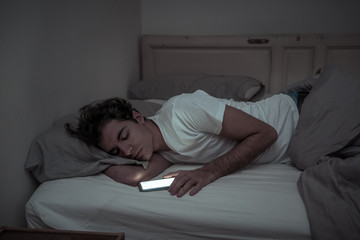 Young man addicted to online social media sleepless surfing on the Internet in bed
