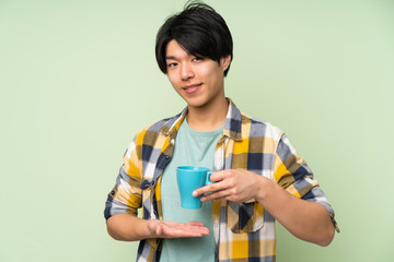 Asian man over isolated green wall holding hot cup of coffee