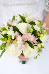 White rose buds in combination with a gray freesia and a sprig of gypsophila in Bouquet of the bride on a blurred background of a wedding dress.