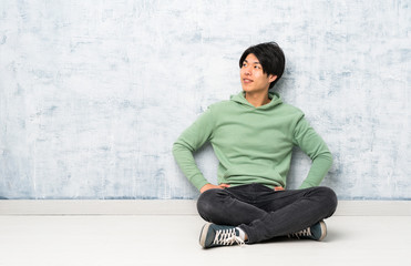 Asian man sitting on the floor posing with arms at hip and smiling