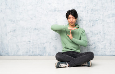 Asian man sitting on the floor making time out gesture