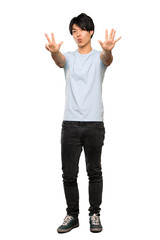 A full-length shot of a Asian man with blue shirt counting eight with fingers over isolated white background