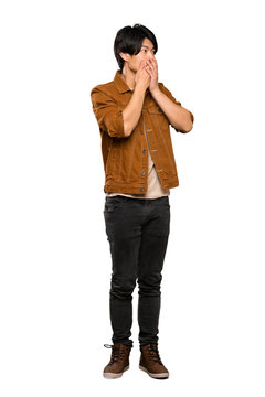 A Full-length Shot Of A Asian Man With Brown Jacket Covering Mouth And Looking To The Side Over Isolated White Background