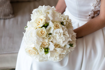Exquisite bridal bouquet of white roses, hydrangeas and freesia in the hands of an unrecognizable bride