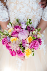 Unrecognizable bride holding a refined wedding bouquet of pink and yellow roses with peonies