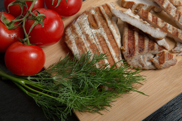 Greens with tomatoes and grilled Turkey steak on a chopping Board. Top view