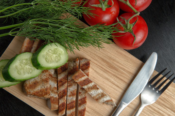 Greens with tomatoes and grilled Turkey steak on a chopping Board. Cutlery on a cutting Board. Top view