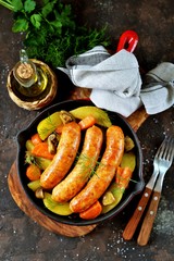 Roast Chicken sausages with potatoes, onions, carrots and mushrooms in a cast-iron pan. Top view. 