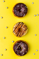 For sweet tooth. Yummy glazed assorted three doughnuts on pastel yellow background. Top view.