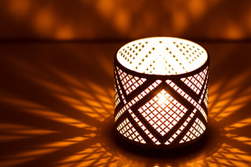 Decorative eastern textured candlestick with burning candle, glowing at night and with glittering golden bokeh lights. Festive greeting card, invitation for the Muslim holy month of Ramadan Hareem. 