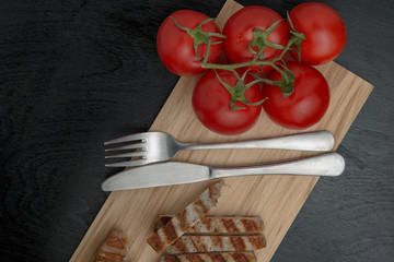 Greens with tomatoes and grilled Turkey steak on a chopping Board. Cutlery on a cutting Board. Top view