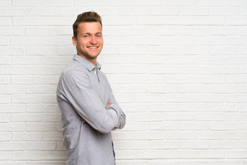 Blonde man over white brick wall with arms crossed and looking forward