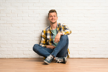 Blonde man sitting on the floor posing with arms at hip and smiling