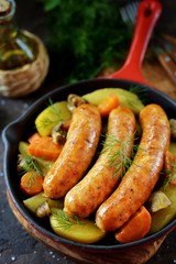 Roast Chicken sausages with potatoes, onions, carrots and mushrooms in a cast-iron pan. Top view. 