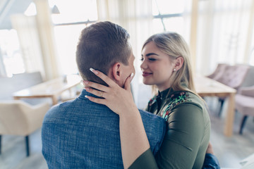 Happy young couple in love on the light baclground. Guy hugging a girl indoor.Romantic relationship in cafe. Happy young man holding his girlfriend in  arms.romantic date in restaurant