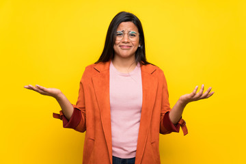 Young Colombian girl over yellow wall making unimportant gesture