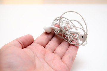 male hands are holding white headphones with tangled wires