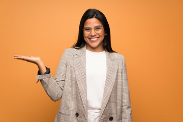 Young Colombian girl over brown wall holding copyspace imaginary on the palm to insert an ad