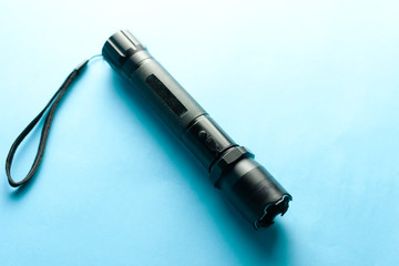 A black metal flashlight with shocker at the blue background. protection and security concept. for design and decoration.