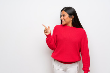 Young Colombian girl with red sweater pointing finger to the side