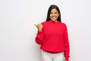 Young Colombian girl with red sweater pointing to the side to present a product