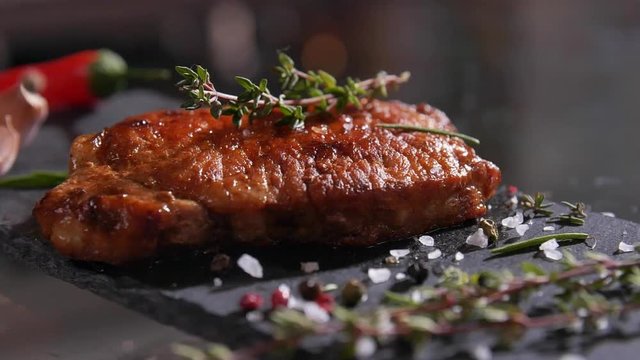 Close-up of salt and pepper falling on the freshly-cooked grilled meat on stone board.