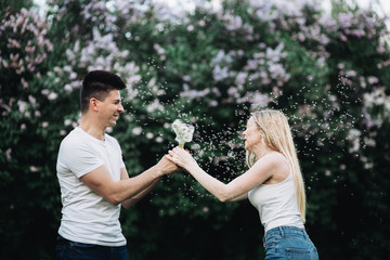 Fototapeta na wymiar A young couple in love holding a dandelion in front of a flowering bush