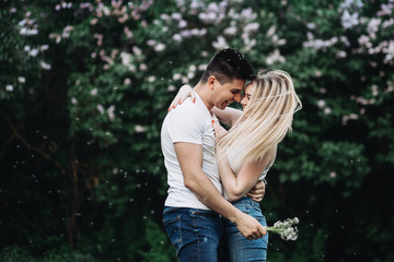 A young couple in love kissing in the park in front of a flowering bush