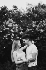 A young couple in love hugging and enjoying the moment in front of a flowering bush in black and white