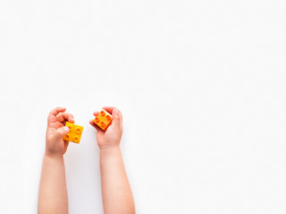 Child is holidng orange and blue constructor blocks in fist. Kid's hands with bricks toy on white background. Educational toy, flat lay, top view.