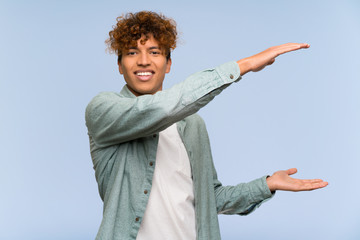 Young african american man over isolated blue wall holding copyspace to insert an ad