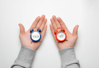 men's hands hold a red and blue alarm clock with the words yes and no. concept of choice and decision making