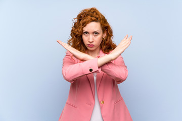 Redhead woman in suit over isolated blue wall making NO gesture