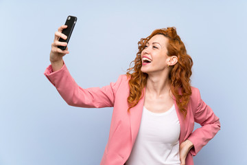 Redhead woman in suit over isolated blue wall making a selfie