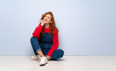 Redhead woman with overalls sitting on the floor thinking an idea while looking up